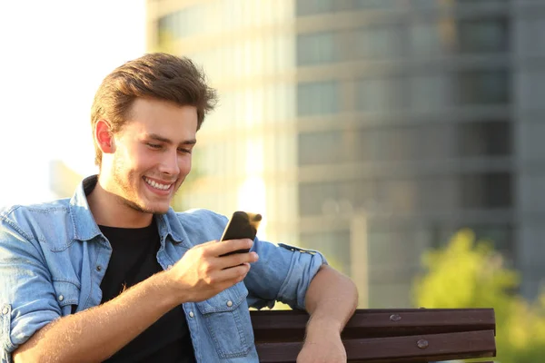 Счастливчик, сидящий на скамейке со смартфоном — стоковое фото