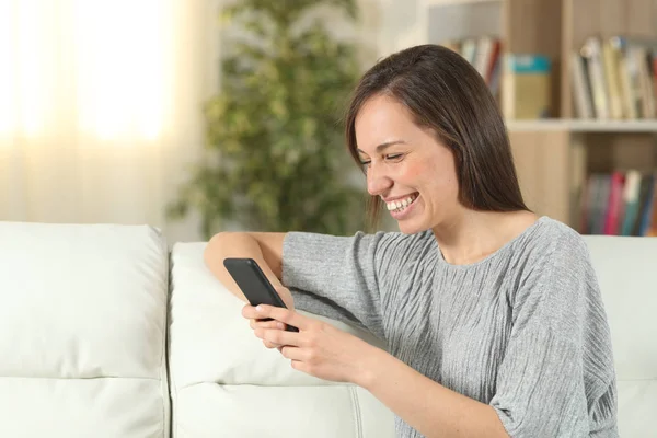 Счастливая женщина дома проверяет смартфон — стоковое фото