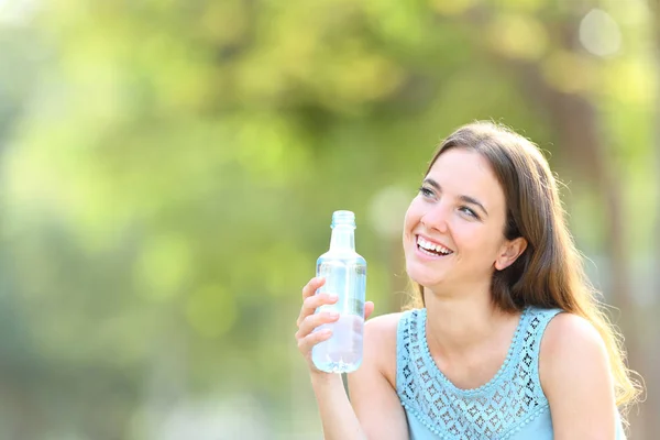 Mulher feliz segurando uma garrafa de água olhando para o lado — Fotografia de Stock