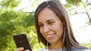 Mutlu yetişkin kadın bir parkta akıllı telefonda müzik dinlerken
