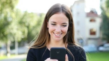 Sokakta çevrimiçi içeriğe göz gezinen bir akıllı telefon kullanarak yürüyen mutlu bir kadının ön görünümü