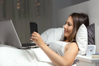 Gece yatakta birden fazla cihaz kullanan kadın