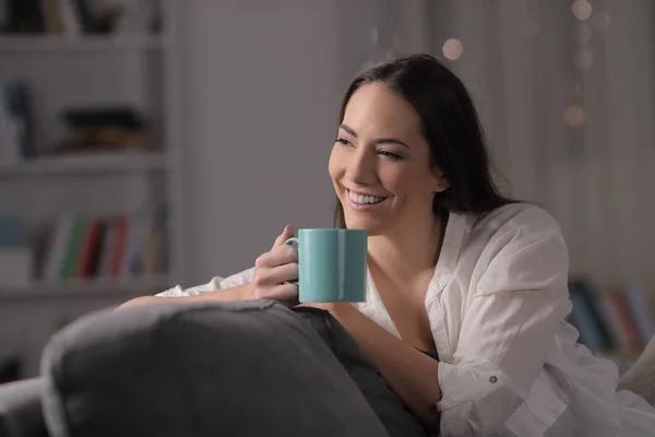Žena v noci pije kávu, která se dívá na bok doma. — Stock fotografie