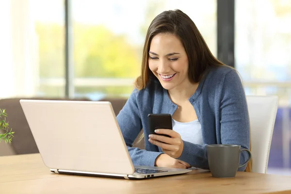 Lycklig kvinna använder telefon och laptop hemma — Stockfoto