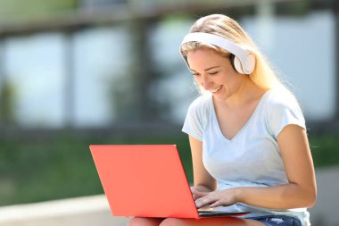 Mutlu genç öğrenci e-dizüstü bilgisayar ve kulaklık kullanarak öğrenme