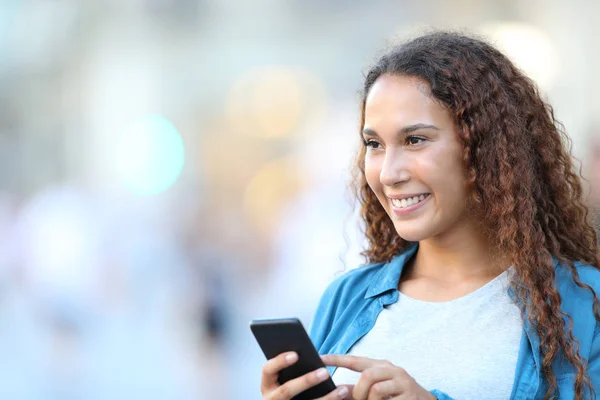 Счастливая женщина смешанной расы смотрит в сторону держа телефон — стоковое фото