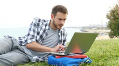 Bir dizüstü bilgisayar kullanarak Sürpriz öğrenci çim üzerinde yatan şaşırtıcı online içerik bulur