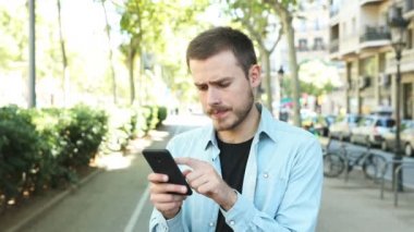 Sinir adam akıllı telefon kullanarak ve sokakta kameraya bakar