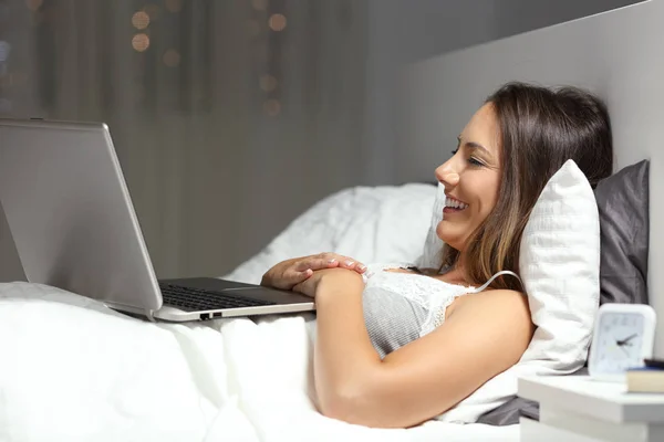 Wanita bahagia menggunakan laptop berbaring di tempat tidur di malam hari — Stok Foto