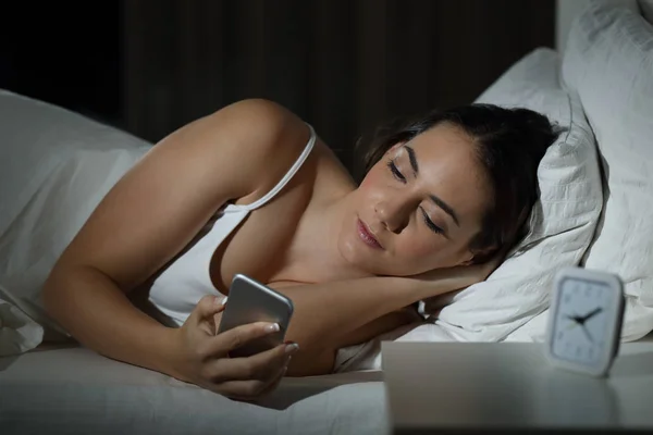 Wanita serius memegang ponsel pintar di tempat tidur — Stok Foto