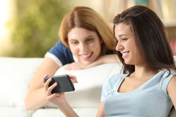 Zwei glückliche Freunde, die zu Hause Medieninhalte am Telefon ansehen — Stockfoto