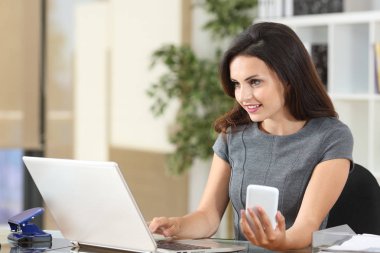 Telefon ve dizüstü bilgisayar kullanarak hat üzerinde çalışan mutlu ofis çalışanı