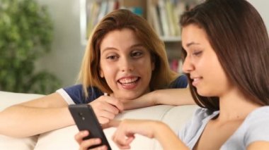 İki mutlu genç arkadaş birlikte livinroom bir kanepede oturan akıllı telefon kontrol 