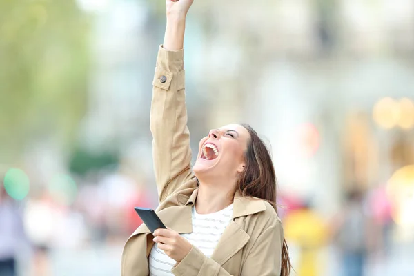 Wanita bersemangat memegang telepon merayakan kabar baik di luar ruangan — Stok Foto