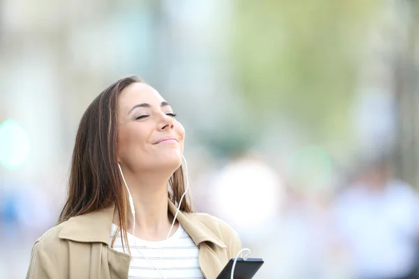 Satisfied woman listening to music in the street — Stock Photo, Image