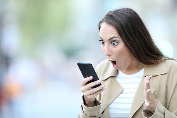 Mujer sorprendida encontrando noticias sorprendentes en el teléfono —  Fotos de Stock