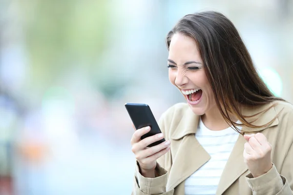 Upphetsad kvinna finner bra erbjudanden på telefon på gatan — Stockfoto