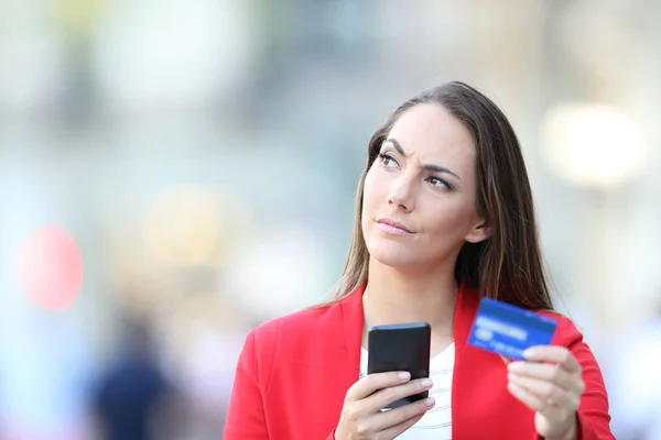 Femme douteuse tenant carte de crédit et téléphone portable — Photo