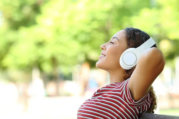 Feliz mujer de raza mixta escuchando música descansando en un parque — Foto de Stock