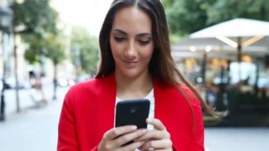 Kameraya doğru yürüyen akıllı telefon kullanarak kırmızı ciddi bir kadının ön görünümü 
