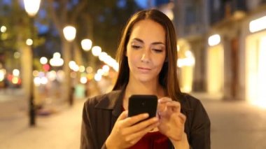 Sokakta akıllı telefon kullanarak gece yürüyen bir kadının ön görünüm portre