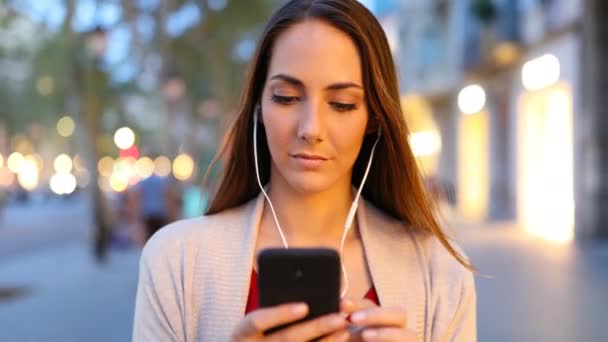 通りで夕方に音楽を聴きながら歩いている女性の正面図 — ストック動画
