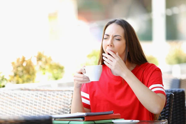 Estudiante cansado bostezando en un bar sosteniendo una taza de café —  Fotos de Stock