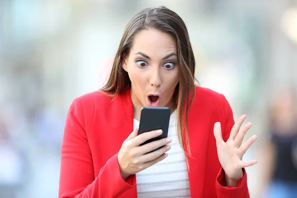 Surprised woman in red checking phone content in the street — Stock Photo, Image