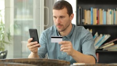 Ciddi adam bir kahve dükkanında çevrimiçi satın almak için bir kredi kartı ve akıllı telefon kullanarak