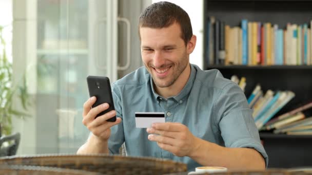 コーヒーショップに座ってカードとスマートフォンでオンラインで購入する幸せな男 — ストック動画