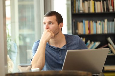 Dizüstü bilgisayar kullanan pensive adam bir barda bir pencereden bakar
