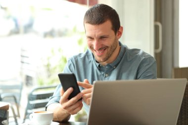 Bir kahve dükkanında telefon kontrol dizüstü bilgisayar ile Mutlu adam