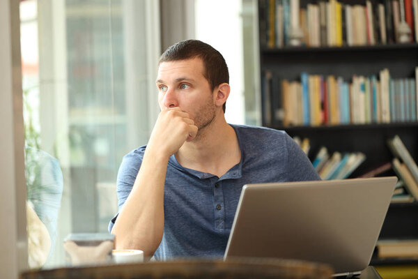 Pensive man using laptop looks through a window in a bar