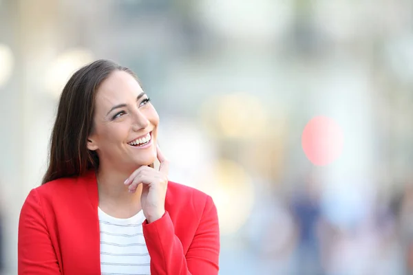 Счастливая женщина в красном думает, глядя на улицу — стоковое фото