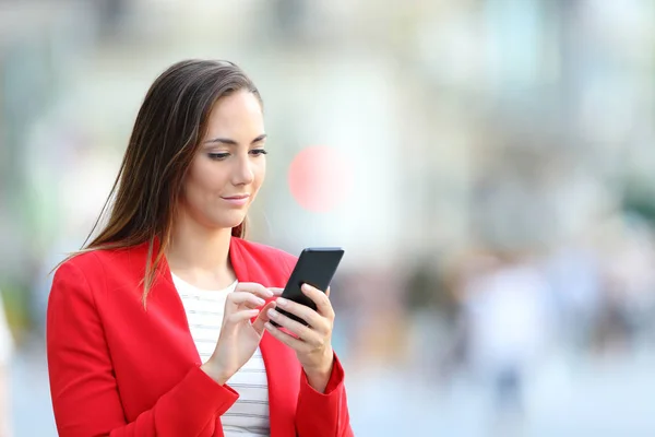 Mujer seria en rojo usando el teléfono inteligente en la calle —  Fotos de Stock