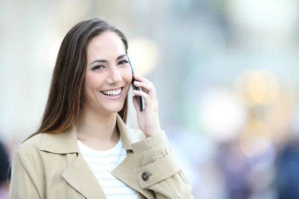 Happy woman talks on phone and looks at you in the street — Stock Photo, Image
