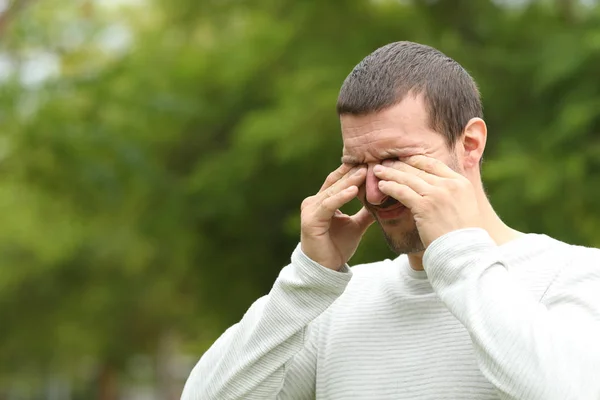 Мужчина, страдающий зудом, царапающий глаза в парке — стоковое фото