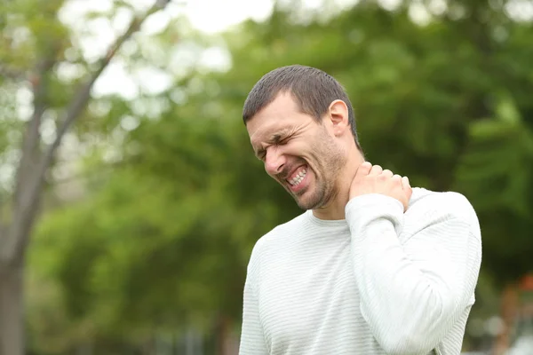 Hombre sufriendo dolor de cuello quejándose en un parque —  Fotos de Stock