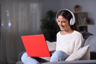 Kulaklık takan mutlu kız geceleri dizüstü bilgisayar kullanıyor.
