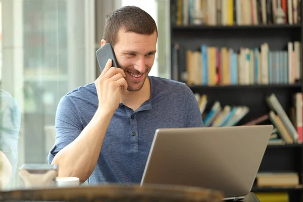 El hombre feliz habla por teléfono comprobando el contenido del portátil en un bar — Foto de Stock