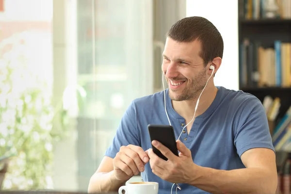 Homem feliz ouvindo música usando telefone inteligente em um bar — Fotografia de Stock