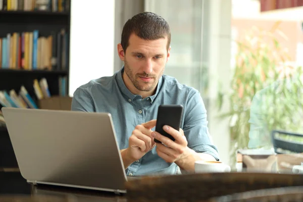 Hombre serio usando teléfono inteligente y portátil en un bar —  Fotos de Stock