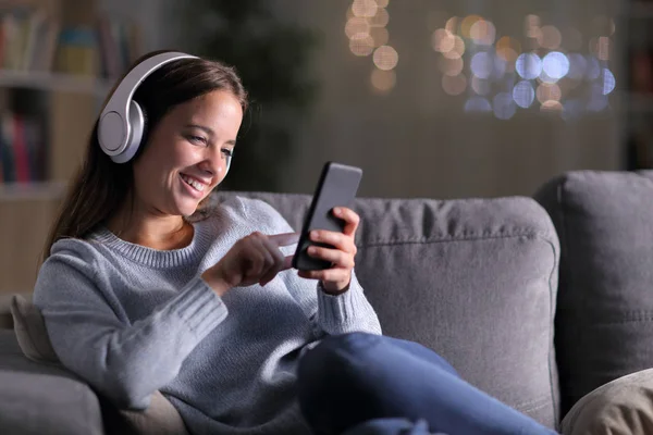 Glad kvinna lyssnar på musik med hjälp av telefon på natten — Stockfoto