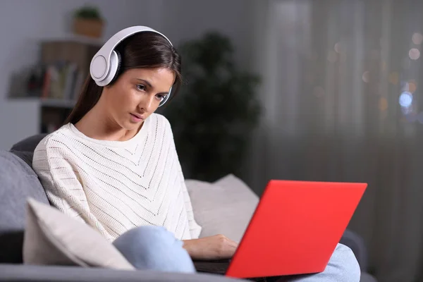 Komoly lány fülhallgatóval ellenőrzi laptop tartalmát az éjszaka — Stock Fotó