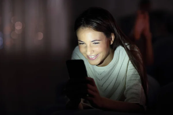 Счастливая девушка проверяет телефон ночью с подсвеченным лицом — стоковое фото