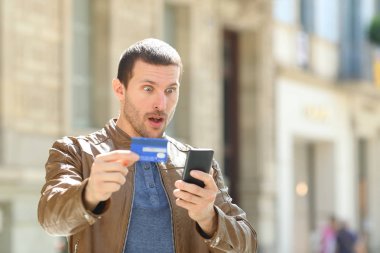 Kredi kartı ve telefonla ödeme yapan şaşırmış bir adam.