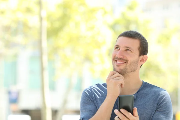 Счастливый взрослый задумчивый мужчина держит телефон смотрит в сторону — стоковое фото