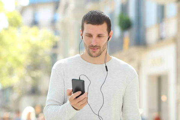 Ciddi bir yetişkin adam sokakta telefonla müzik dinliyor. — Stok fotoğraf