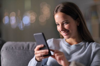 Mutlu kadın gece evde akıllı telefon kullanıyor.