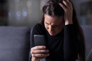 Üzgün kız karanlıkta cep telefonundan kötü haberleri kontrol ediyor.